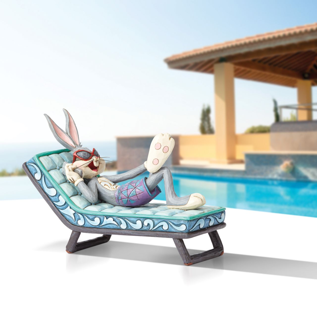 Movie mogul Bugs Bunny catches some rays in this whimsical scene from Looney Tunes. Handcrafted in rich detail, this poolside rabbit is beautifully decorated with the quilt patterns and folk-art style that are unmistakably Jim Shore.