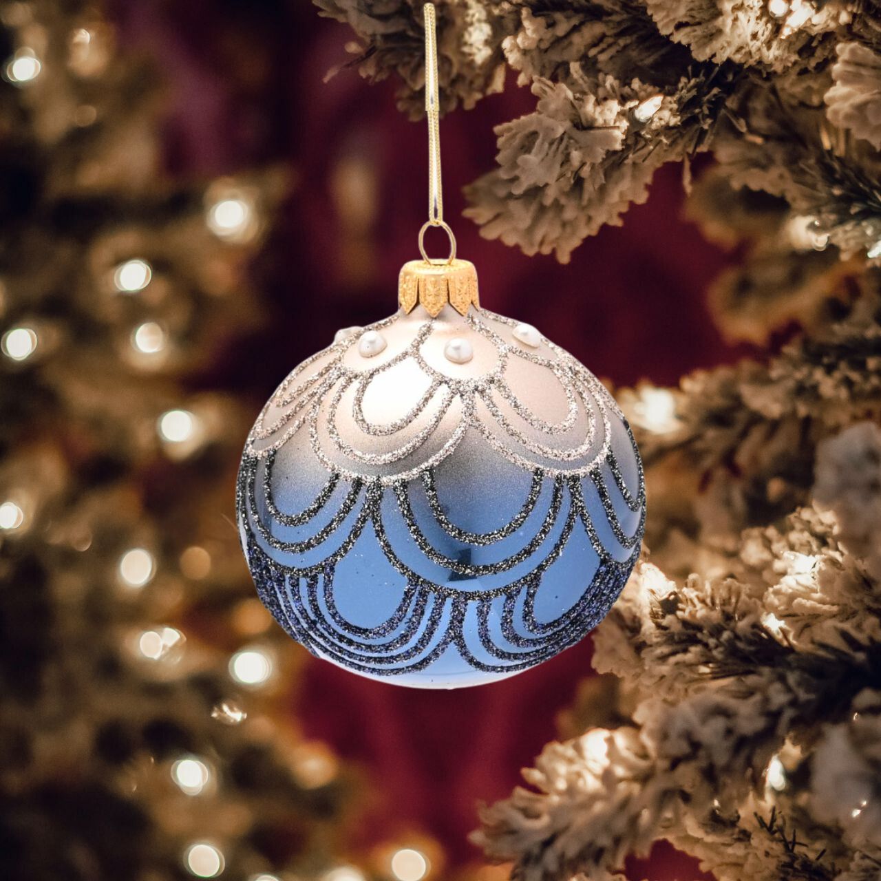 The glass bauble showcases attractive blue &amp; silver colouring, complete with hand decorated ornate embellishments and a shiny glitter finish. It is displayed on the tree using its gold thread.