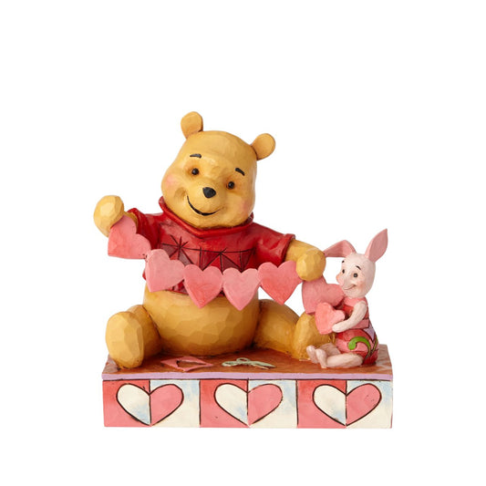 Disney Traditions Handmade Valentines Pooh and Piglet Figurine  Will you be Pooh's Valentine? Piglet and Winnie the Pooh sit close beside each other as they trace and snip a handmade garland of hearts. Folk art-inspired details add to the artisanal charm of this hand-painted figurine, sculpted from high-quality cast stone.