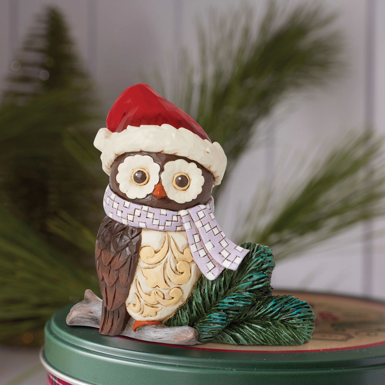 This miniature owl figurine wears a patchwork blue scarf with a Santa hat. With wide eyes and sweet expression, the little owl perches near pine needles with a rosemaling bust. This charming Jim Shore figurine is sure to make your holidays a hoot!