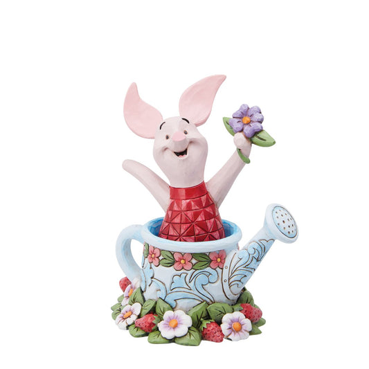 Piglet in a Watering Can Figurine  Introducing the delightful Piglet in a Watering Can Figurine from Disney Traditions by Jim Shore. Dressed in his signature pink jumper, this lovable character is holding a beautiful, pastel purple flower in his hand. This charming figurine is whimsical and heart-warming, bringing joy and magic to any collection of Disney figurines.