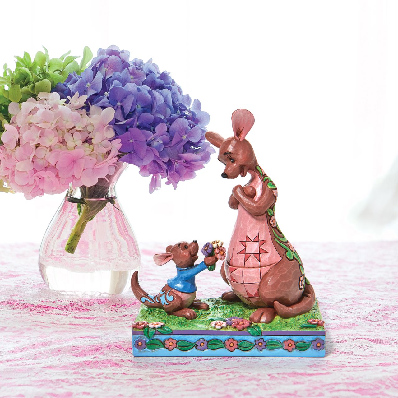 "The Sweetest Gift" The Winnie the Pooh crew enjoy Spring in the Hundred Acre Wood. Kanga and Roo pick wild flowers in the crisp morning air. Engraved with flowers and patchwork, the Jim Shore modelled kangaroo accepts her joey's freshly picked gift with a smile.