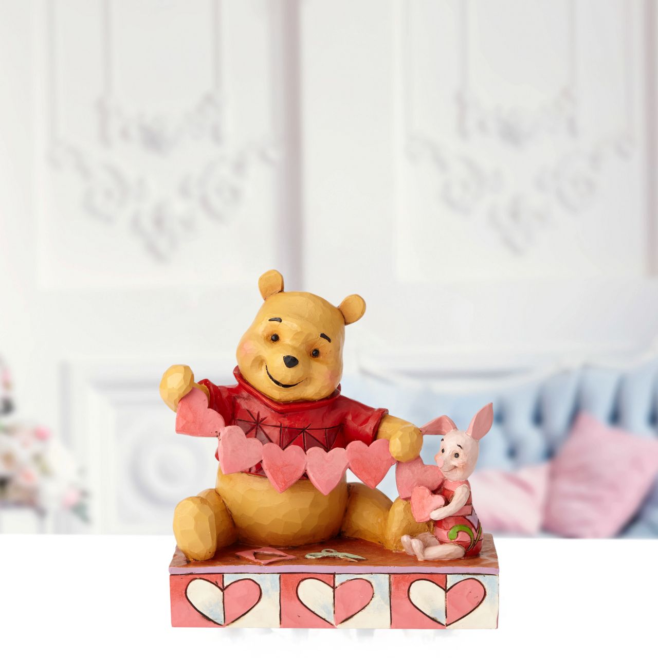 Disney Traditions Handmade Valentines Pooh and Piglet Figurine  Will you be Pooh's Valentine? Piglet and Winnie the Pooh sit close beside each other as they trace and snip a handmade garland of hearts. Folk art-inspired details add to the artisanal charm of this hand-painted figurine, sculpted from high-quality cast stone.