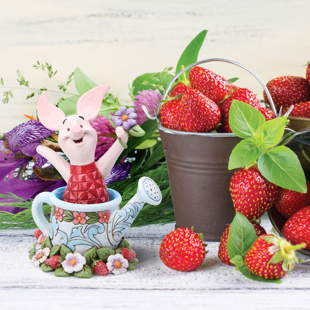 Piglet in a Watering Can Figurine  Introducing the delightful Piglet in a Watering Can Figurine from Disney Traditions by Jim Shore. Dressed in his signature pink jumper, this lovable character is holding a beautiful, pastel purple flower in his hand. This charming figurine is whimsical and heart-warming, bringing joy and magic to any collection of Disney figurines.