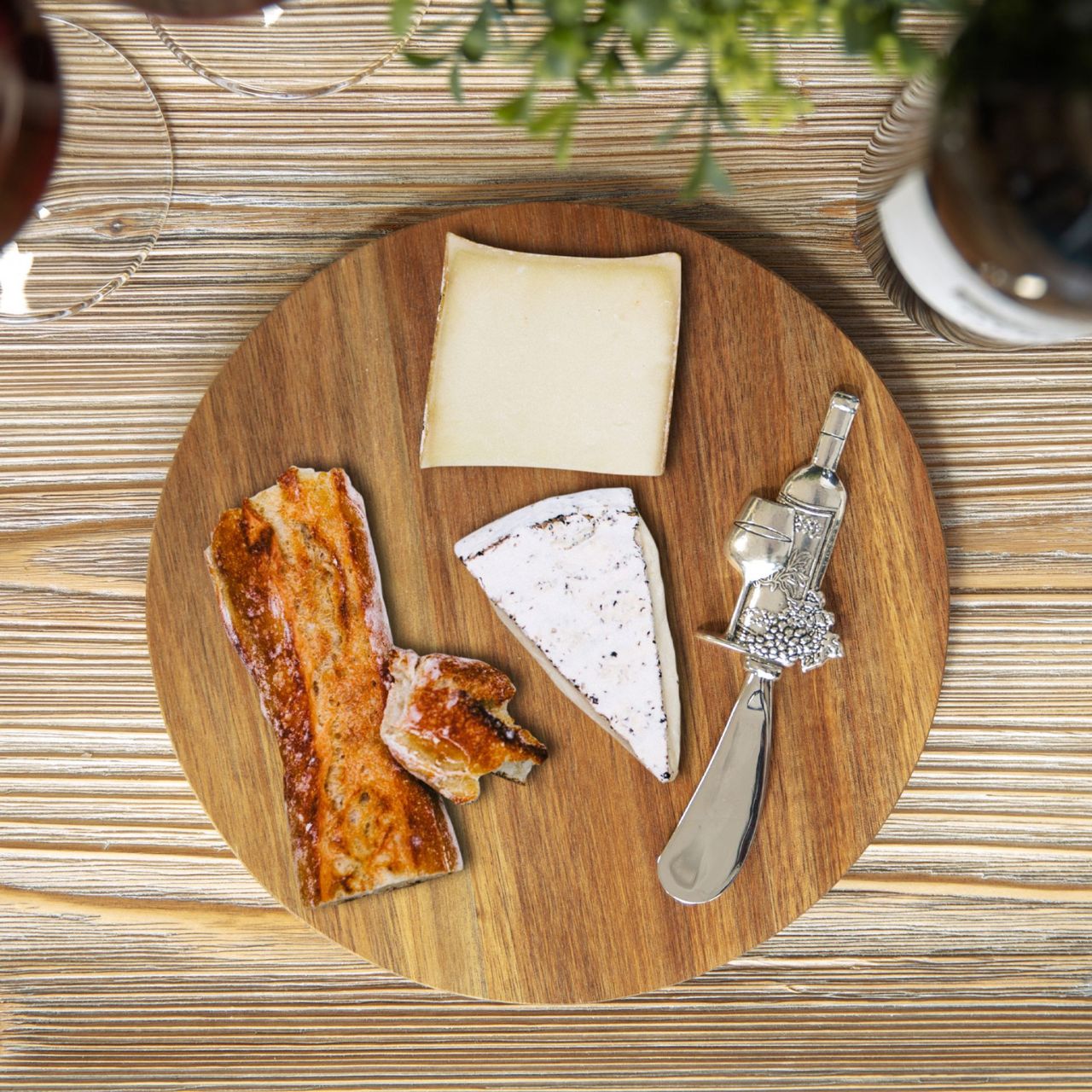 A beautiful round acacia wood cheese board with wine themed stainless steel cheese spreader in a branded gift box.