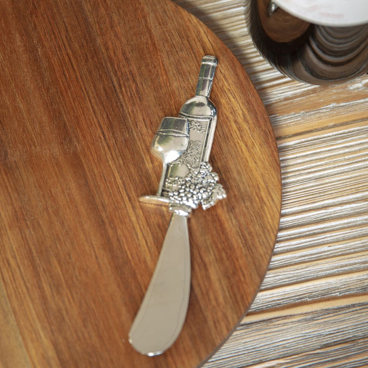 A beautiful round acacia wood cheese board with wine themed stainless steel cheese spreader in a branded gift box.