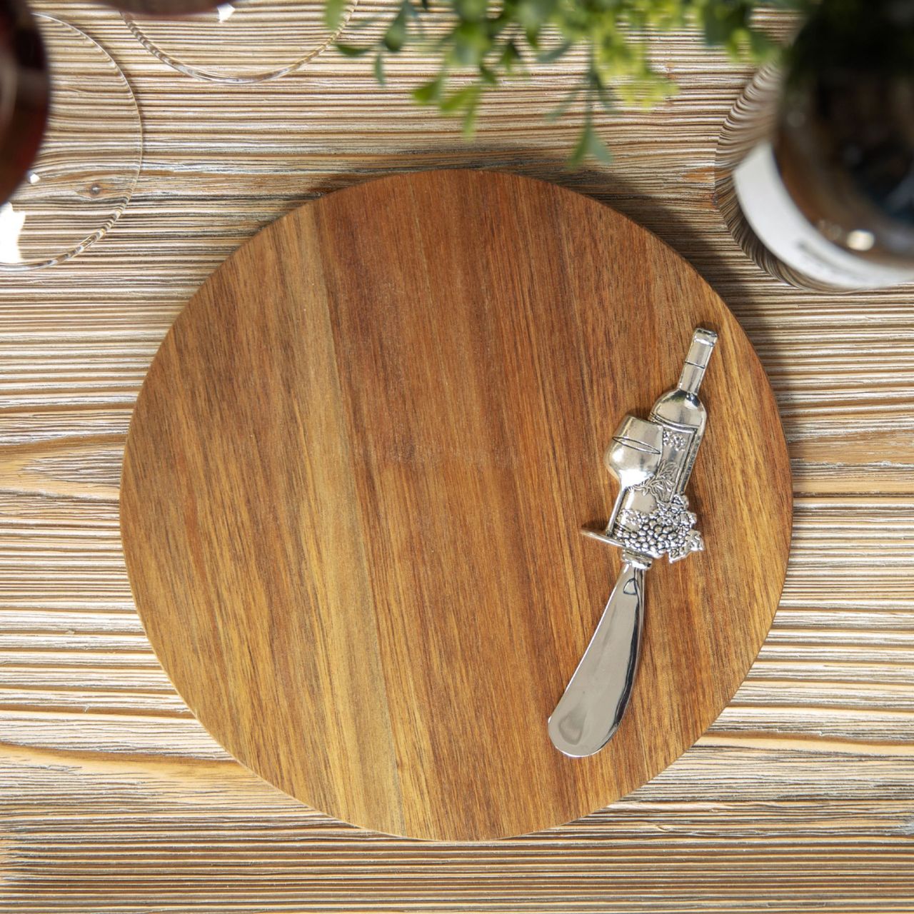 A beautiful round acacia wood cheese board with wine themed stainless steel cheese spreader in a branded gift box.