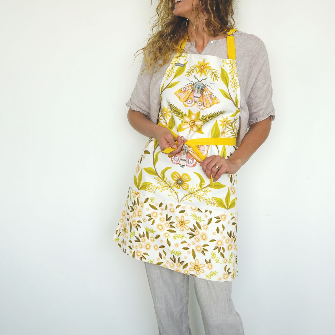 White Moth Apron by Allen Design  Our White Moth adjustable apron is made from 100% cotton and sturdy, canvas material. The fabric is certainly durable, yet flexible enough for every day comfort. The fully adjustable neck strap makes these adult-sized aprons are perfect for anyone. Each one has a recycled cardboard branded strap. Exclusively designed by Michelle Allen.